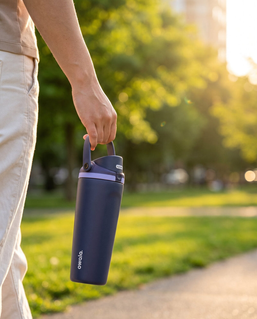 Mano llevando una botella Owala azul por el asa en un parque